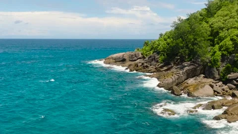 Green hills and rocky cliffs by turquoise ocean waves. Seychelles, Mahe. Stock Footage 323149783