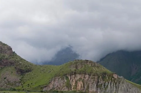 Green hills at the deep dramatic mist. Light greenery hill with rocks Stock Photos
