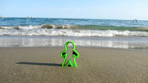 Green human shaped plastic figures buried into the sea sand Stock Photos