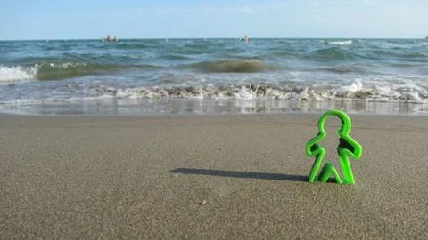Green human shaped plastic figures buried into the sea sand Foto stock