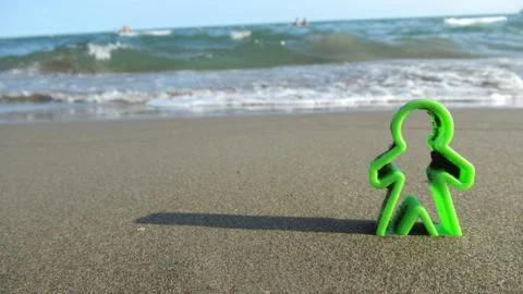 Green human shaped plastic figures buried into the sea sand Stock Photos