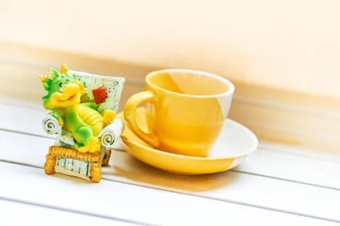 A green imp is drinking coffee next to a yellow cup Stock Photos