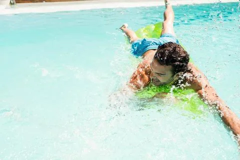 Green inflatable float bobbing, splashing water on turquoise pool in bright Stock Photos