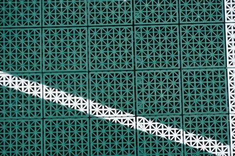 Green interlocking plastic tiles with a white line marking viewed from above Stock Photos