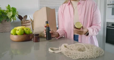 Green-jacket person is pulling celery from paper bag while woman is moving jars, Stock Footage 342023568