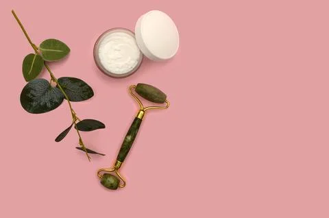 Green jade roller and eucalyptus branch on a pink background. Stock Photos
