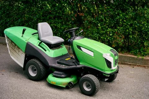 Green large lawn mower stands on the asphalt near the bushes Stock Photos