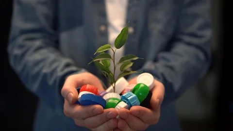 Green leaf of sprout growing in the hands of colorful plastic bottle caps Stock Footage 124898542