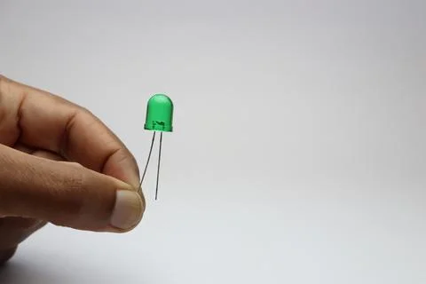 Green light emitting diode or LED held in the hand by its connecting pin Stock Photos
