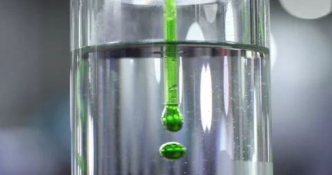 Green liquid drops falling into clear fluid during laboratory testing process Stock Footage 346704632