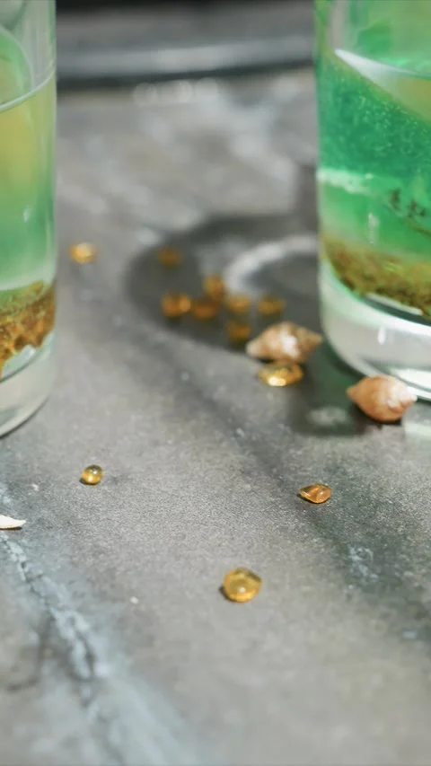 Green liquid in glass with glitter and seashells on gray surface closeup showing Stock Footage 344678261