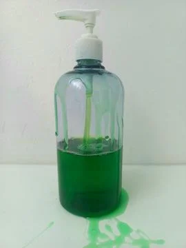 Green Liquid Soap Leaking Down Transparent Pump Bottle on White Table Stock Photos