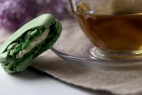 Green macaron is placed next to a cup of tea on a table with soft colors in the Fotos Stock