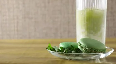 Green macarons rest on a plate next to a glass of mint drink on a wooden table Stock Photos