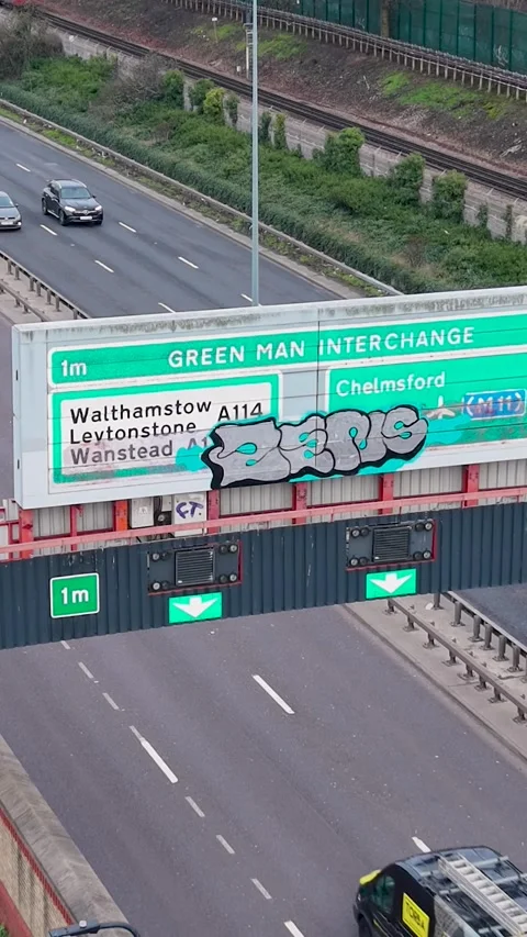 Green Man interchange A12 sign with graffiti, vertical drone reverse rise in Stock Footage 331271832