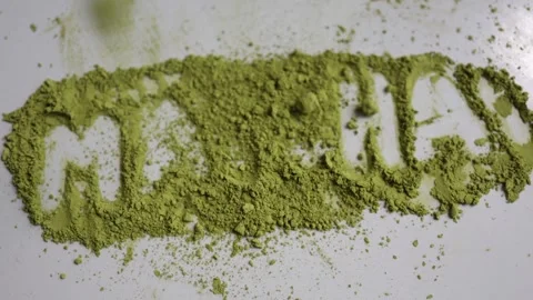 Green matcha powder falls over the matcha word creating a dynamic food concept Видео 344044208
