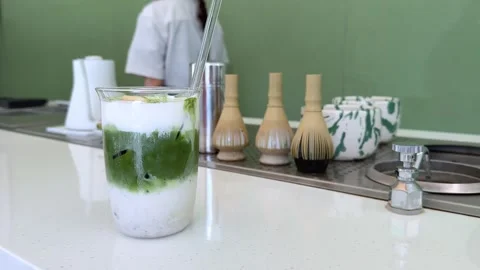 Green matcha tea being poured from a white pitcher into a clear glass mug Stock Footage 312266093