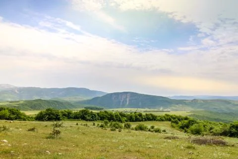 Green meadow on the background with distant mountains. Open field with green Stock Photos