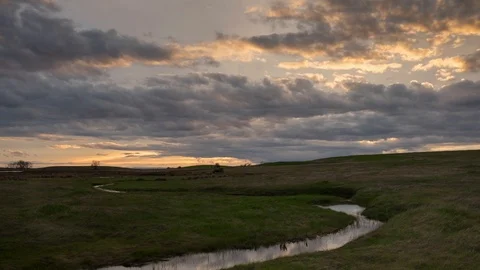 Green Meadow With A Creek Under A Sunset Sky With Clouds - 4k Timelapse Stock Footage 106157331
