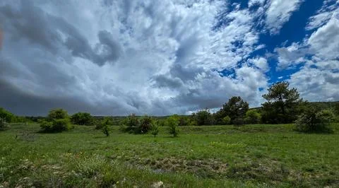 Green meadow landscape under dramatic storm clouds and blue sky with trees an Stock Photos