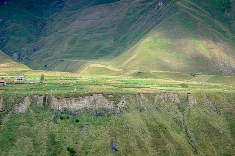 Green mountain slopes with fields haystacks and small houses in rural area Stock Photos