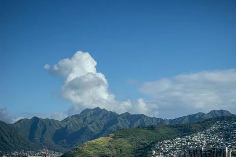 Green mountains with dense clouds above peaks and city below Stock Photos