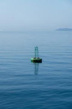 Green navigation buoy floating on calm blue sea Stockfoto's