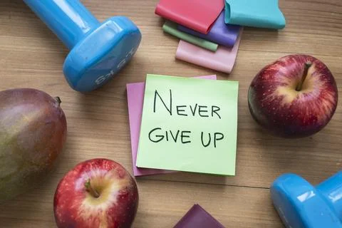 Green Never Give Up Sticky Note Surrounded by Fresh Fruit and Fitness Acces.. Stock Photos