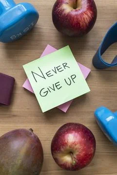 Green Never Give Up Sticky Note Surrounded by Fresh Fruit and Fitness Acces.. Stock-Fotos