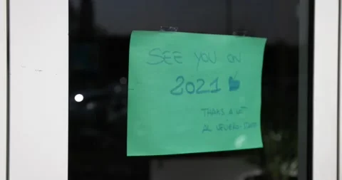 Green note on a door see you in 2021 closed because of covid 19 pandemic pan Stock Footage 150389725
