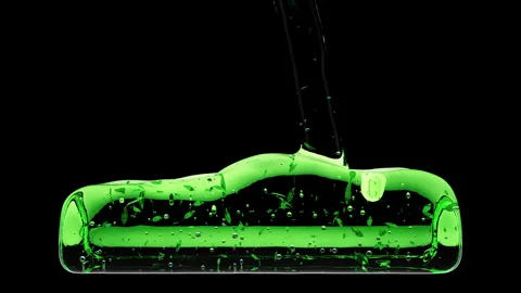 Green oily liquid with bubbles and leaves flowing down into transparent bottle Stock Footage 267029196