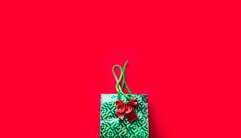 Green package with a present and a bow on a red background with copyspace. A  Foto stock