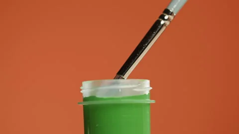 Green paint isolated on orange background. Bright gouache falling from Stock Footage 178596433