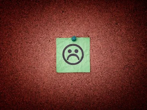 A green paper note with sad face on a cork board. Stock Photos