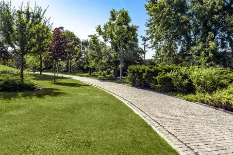 Green parkland with neatly mowed lawn and paved path on summer day Stock Photos