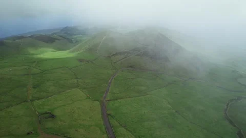 Green patchwork pastureland surround volcanic cones as drone flies into clouds Stock Footage 303346816