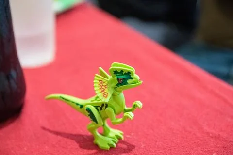 Green patterned toy dinosaur on red surface under natural light Stock Photos