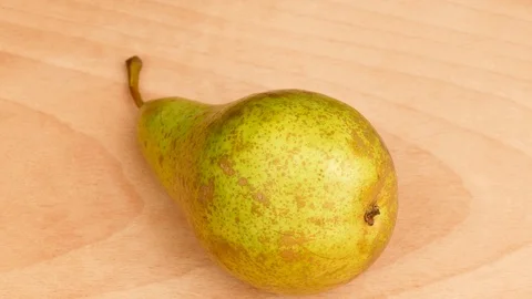 Green pear rotates around its own axis on a wooden stand. Stock Footage 107730404