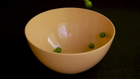 Green peas falling into pale orange bowl on black background 4k 120fps Stockbeeldmateriaal 333698525