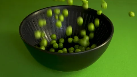 Green peas macro falling into black bowl on green background 4k 120fps Stockbeeldmateriaal 333720895