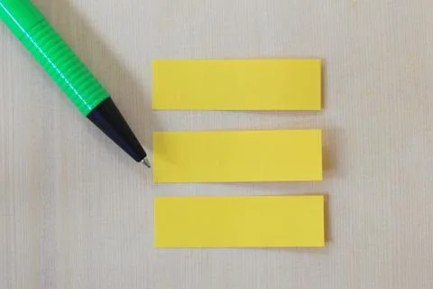 Green pen pointing to empty yellow paper note on wooden floor background. Stock Photos