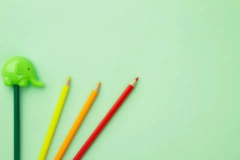 Green pencil sharpener in the form of an elephant and four pencils on a pale  Stock Photos