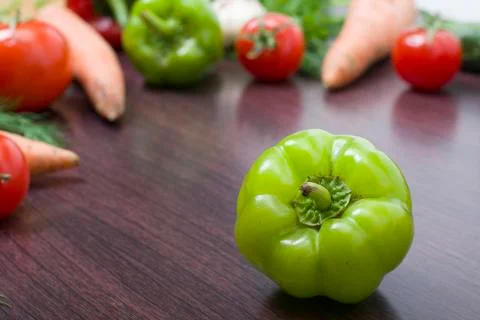 The green peppers on a table on the background of vegetables. Fresh tomatoes Stock Photos