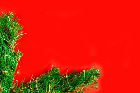 Green pine branches with light bulbs on a red background frame the corner of the Stock Photos