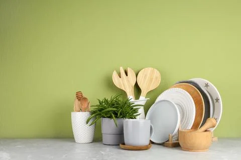 Green plant and different kitchenware on table near color wall, space for tex Stock Photos