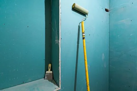 Green plasterboard or drywall and yellow roller for painting gypsum walls in Stock Photos