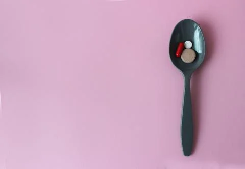 Green plastic spoon with colored tablets on a pink background. Medical concept. Stock-Fotos