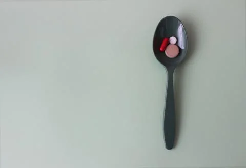 Green plastic spoon with colored tablets on a green background. Medical concept. Stock Photos