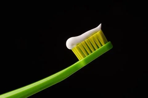 Green plastic toothbrush with white toothpaste on a black background. Stock Photos