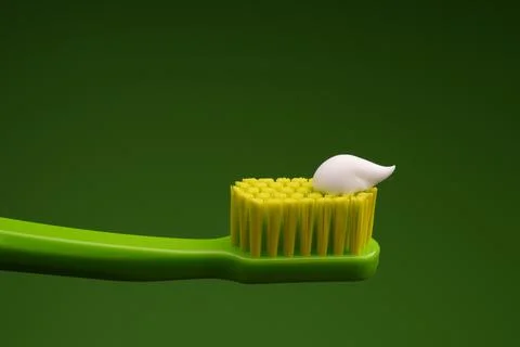 Green plastic toothbrush with white toothpaste on a green background. Stock Photos
